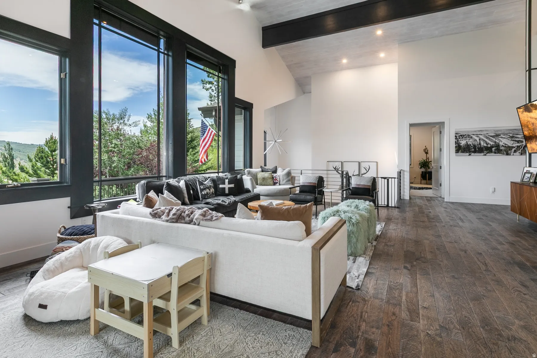 Spacious living area featuring large picture windows, wood-finish flooring, a vaulted ceiling with exposed beam, and recessed lighting