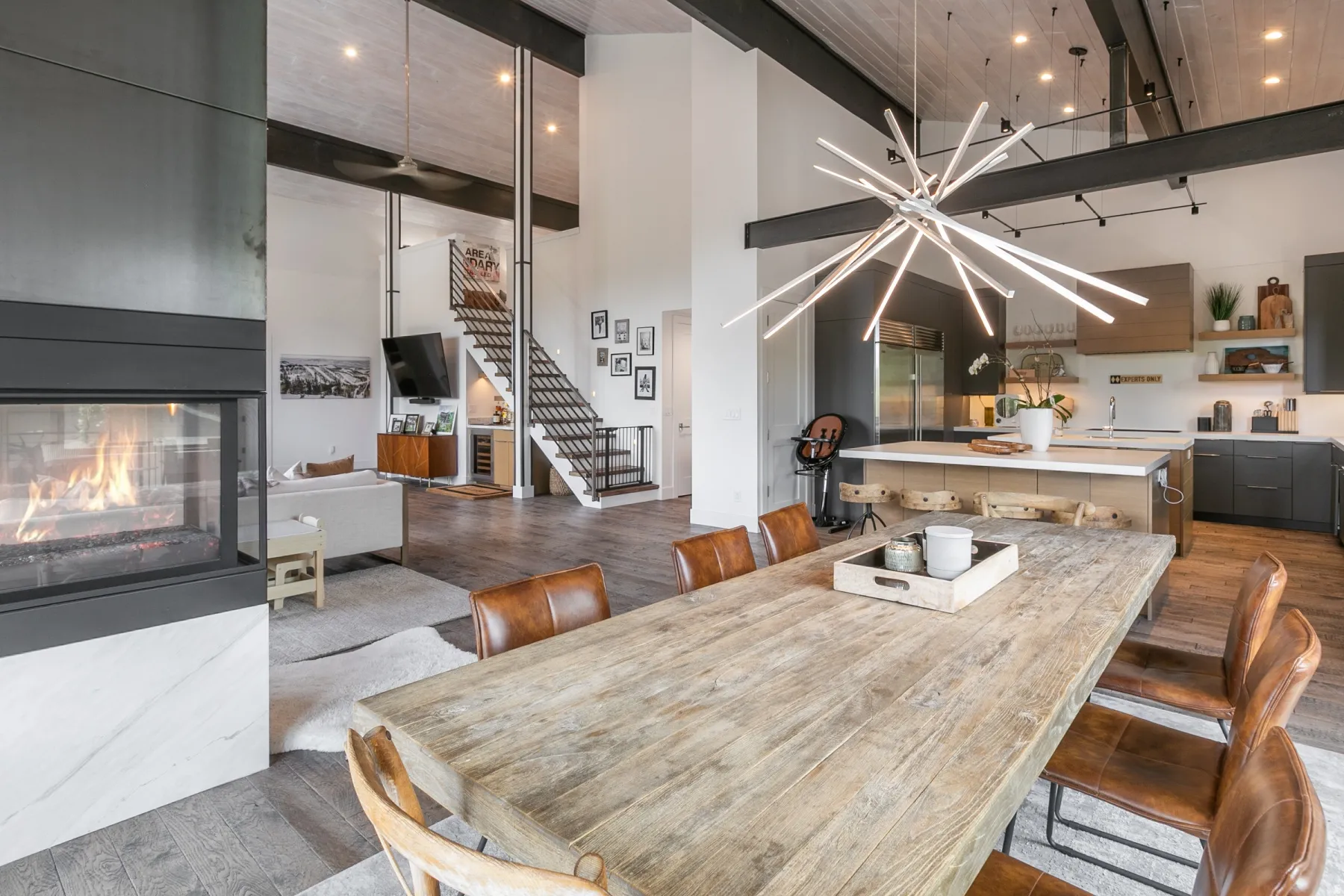 Contemporary open-concept living space featuring a linear gas fireplace with a stone surround, a floating staircase with metal railings, and wood-finish flooring
