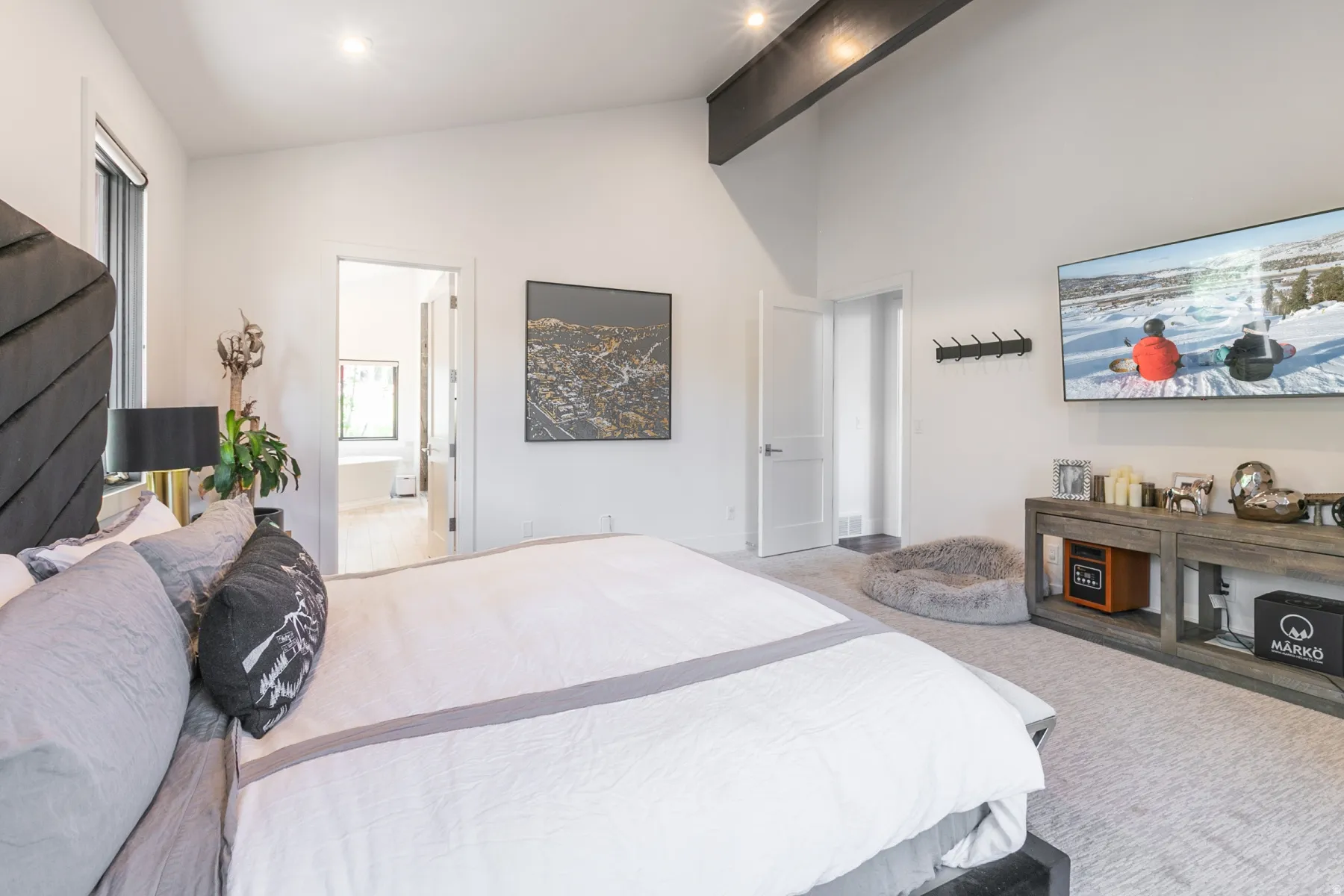 Spacious bedroom featuring high ceilings with exposed beams, light-toned carpeting, and a large window