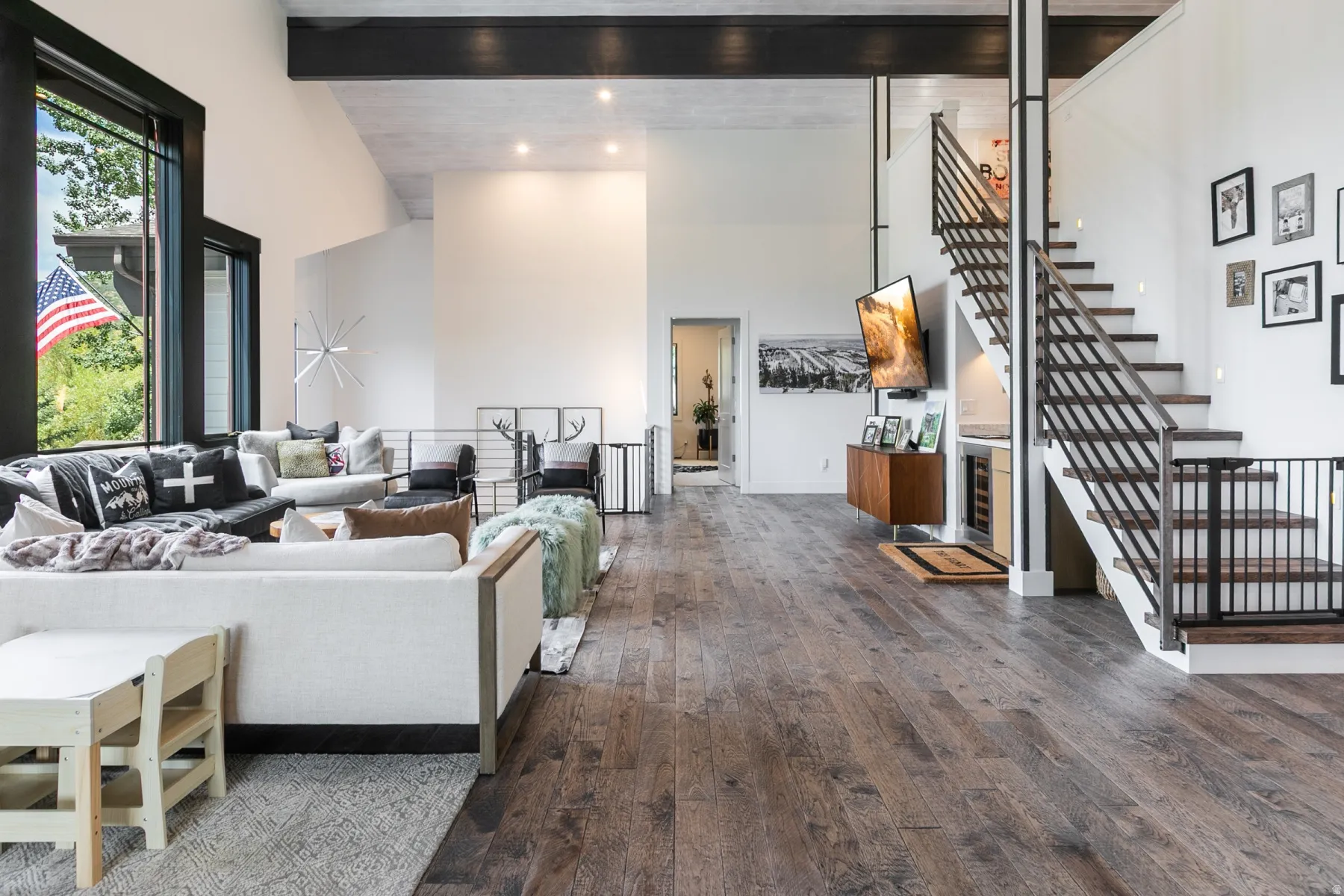 Spacious interior featuring wood-finish flooring, vaulted ceilings with exposed beams, and a modern open staircase with metal railings