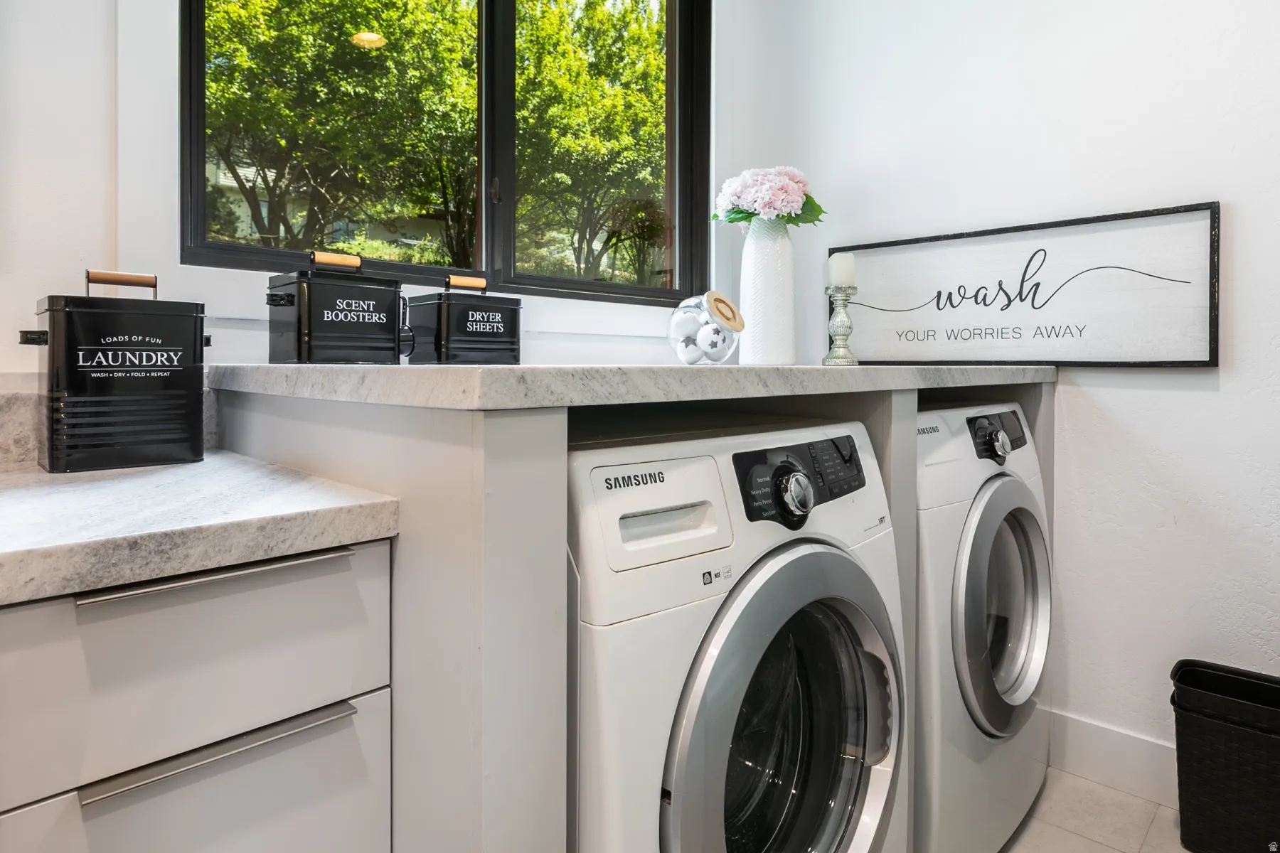 Dedicated laundry area featuring a built-in countertop, light-toned cabinetry with modern hardware, and a large window providing natural illumination