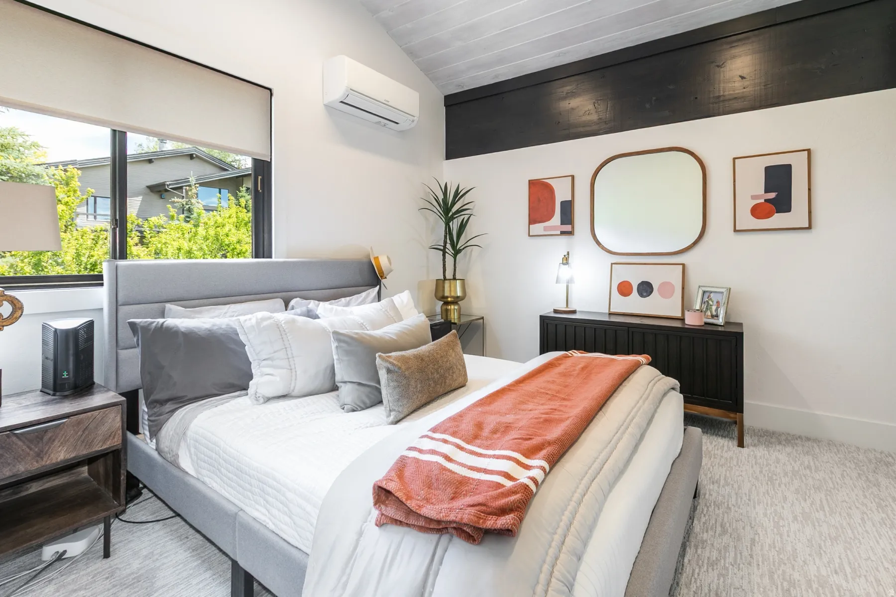 Vaulted ceiling with wood-finish planks, large window with roller shade, upholstered headboard, and a built-in credenza