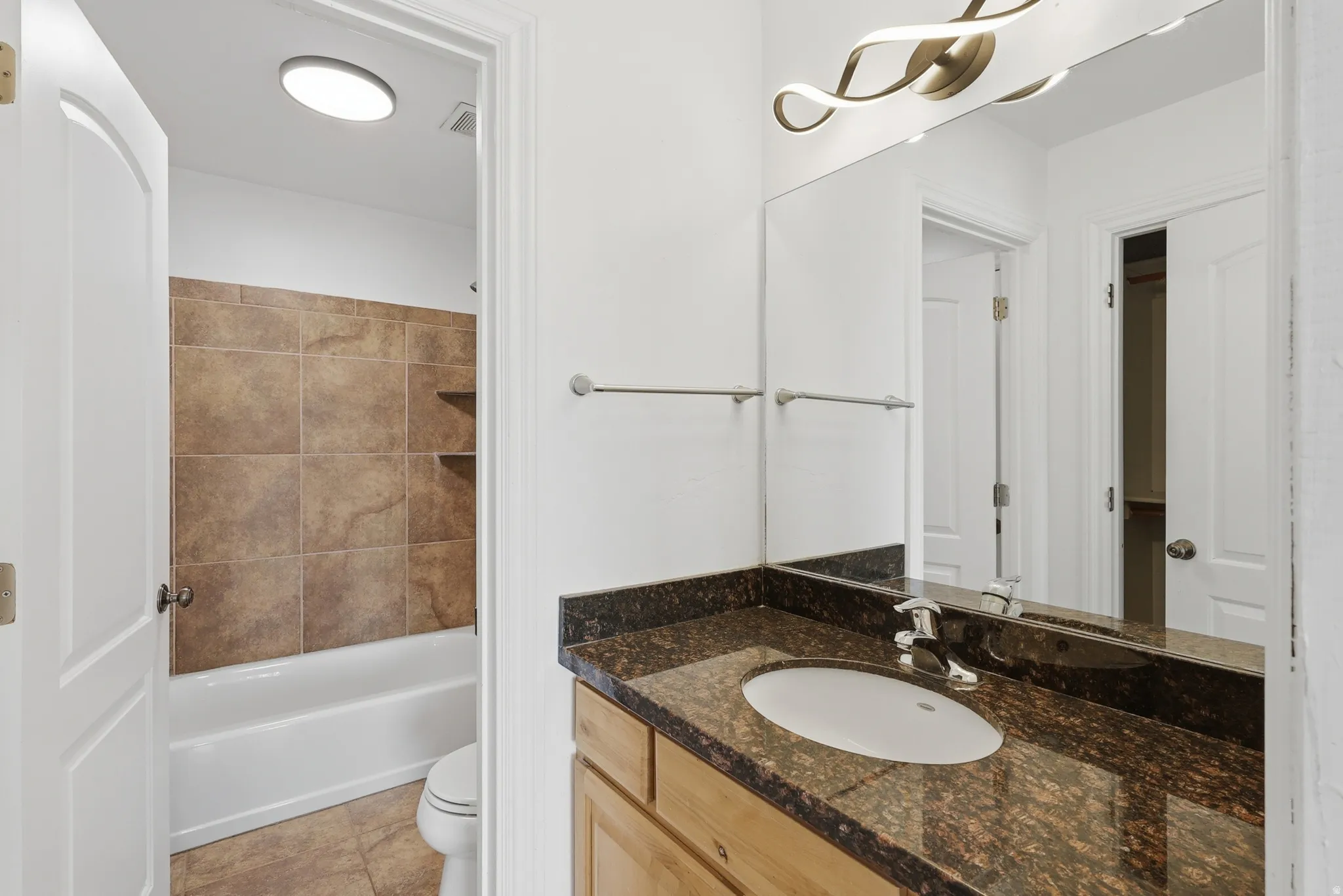 Bathroom vanity featuring a dark granite countertop, undermount sink, and contemporary vanity lighting