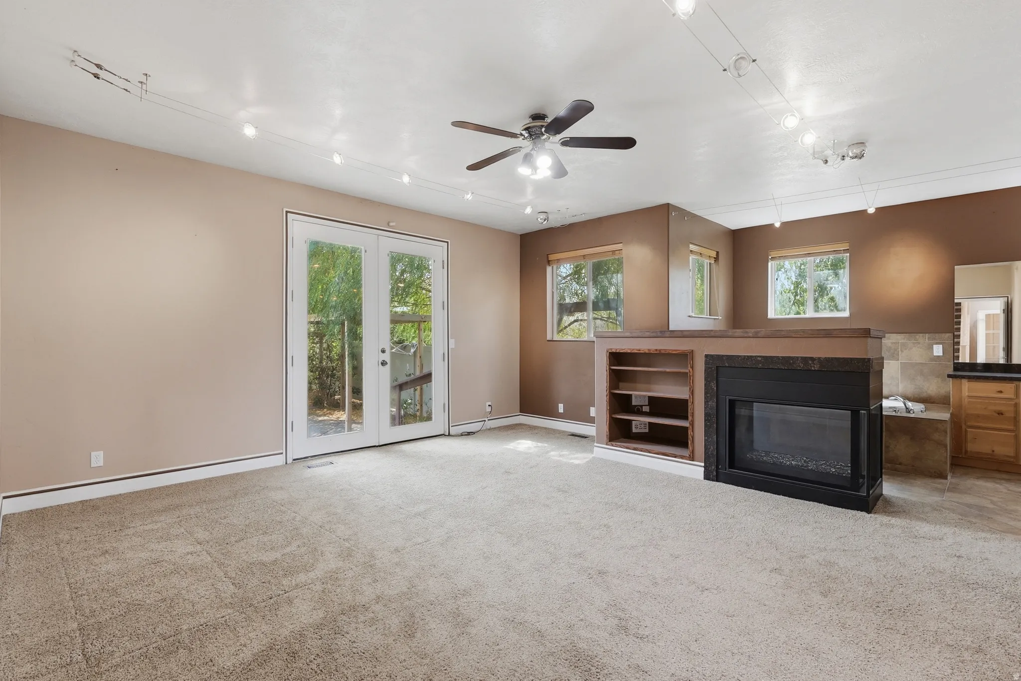 Living area featuring a ceiling fan, track lighting, and a built-in fireplace with an integrated shelving unit