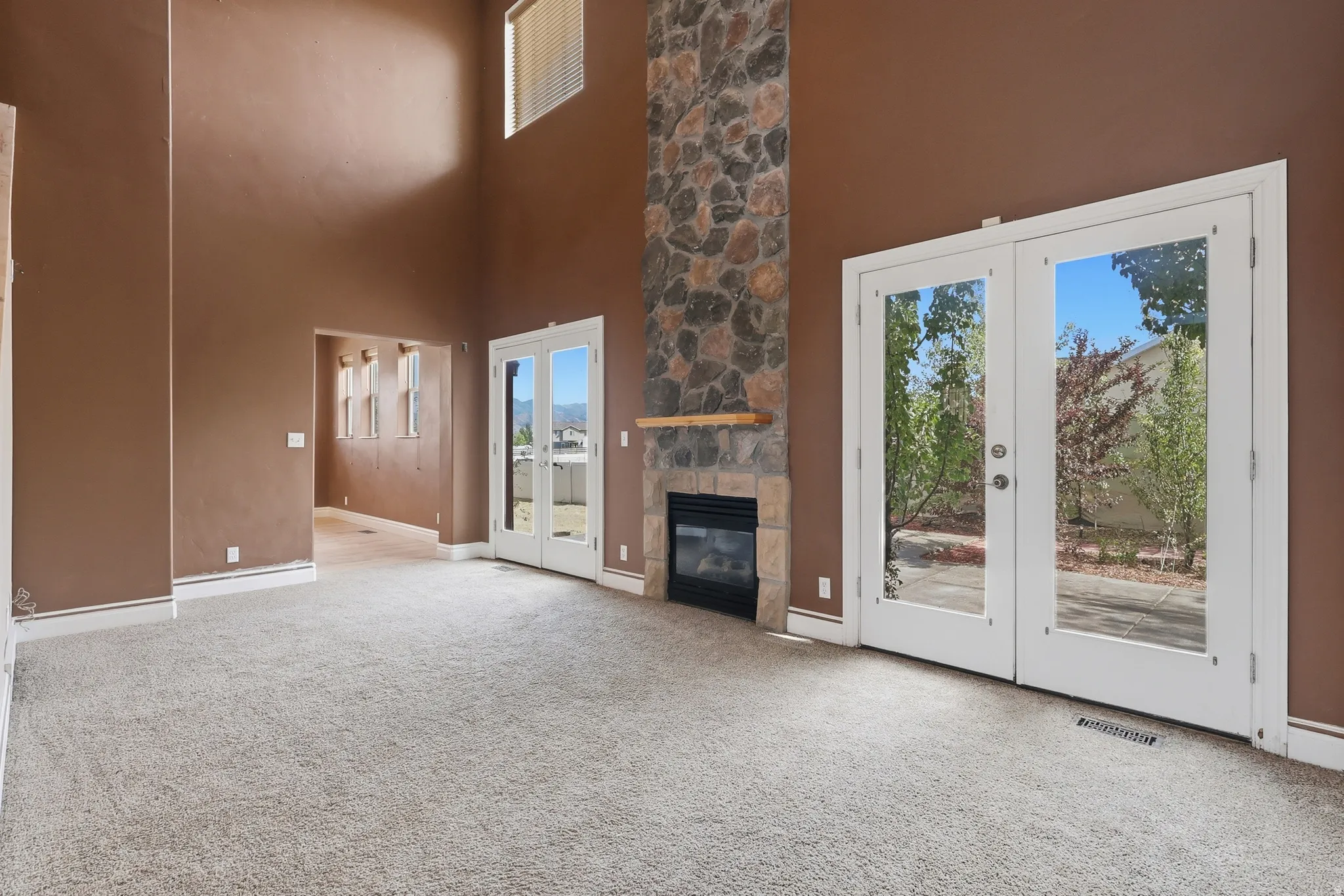 Spacious living area featuring a floor-to-ceiling stone fireplace, high ceilings, carpeted flooring, and exterior access via double French doors