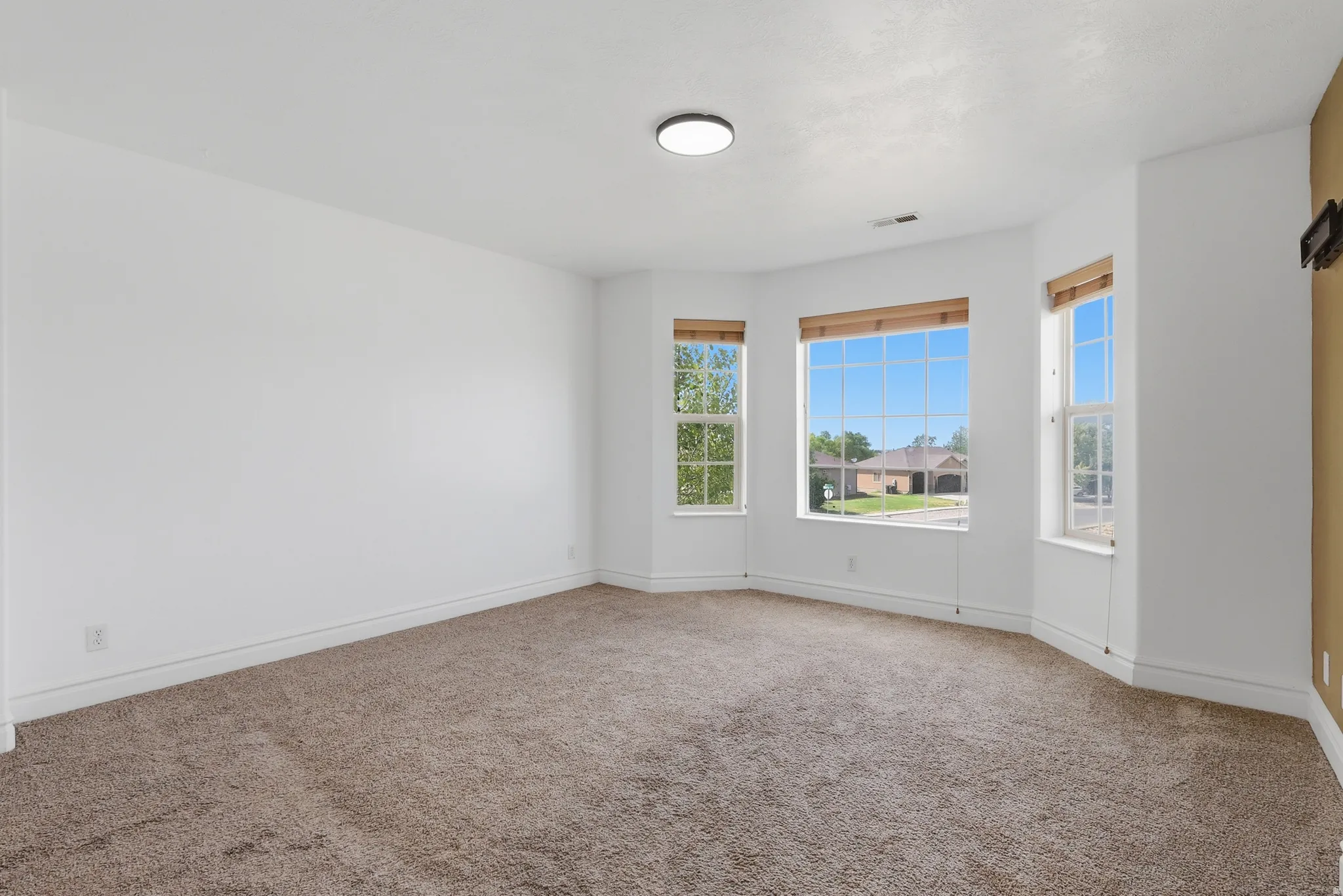 Spacious room featuring a bay window with three large windows, neutral-toned carpet, white painted walls, and a contemporary ceiling light fixture
