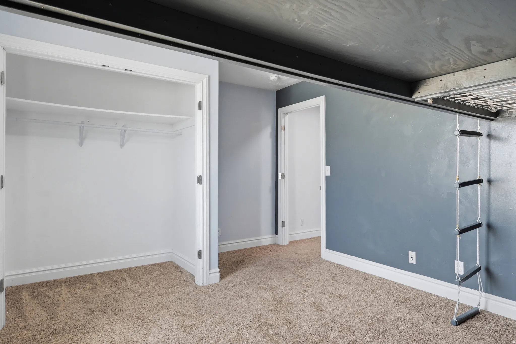 Interior space featuring a built-in closet with shelving, overhead loft structure, rope ladder, and neutral carpeting