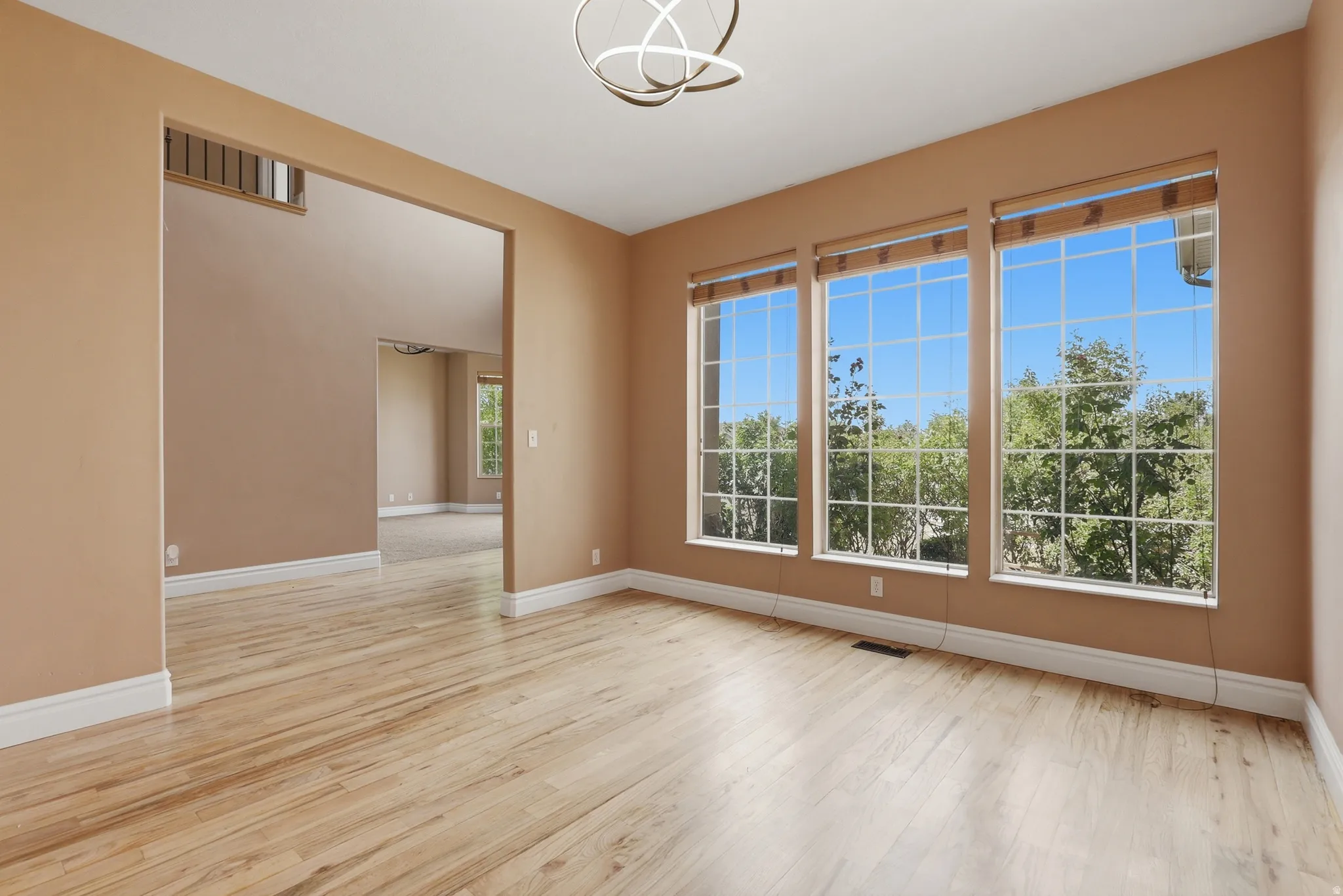 Bright living space featuring three large windows, wood-finish flooring, and a contemporary light fixture