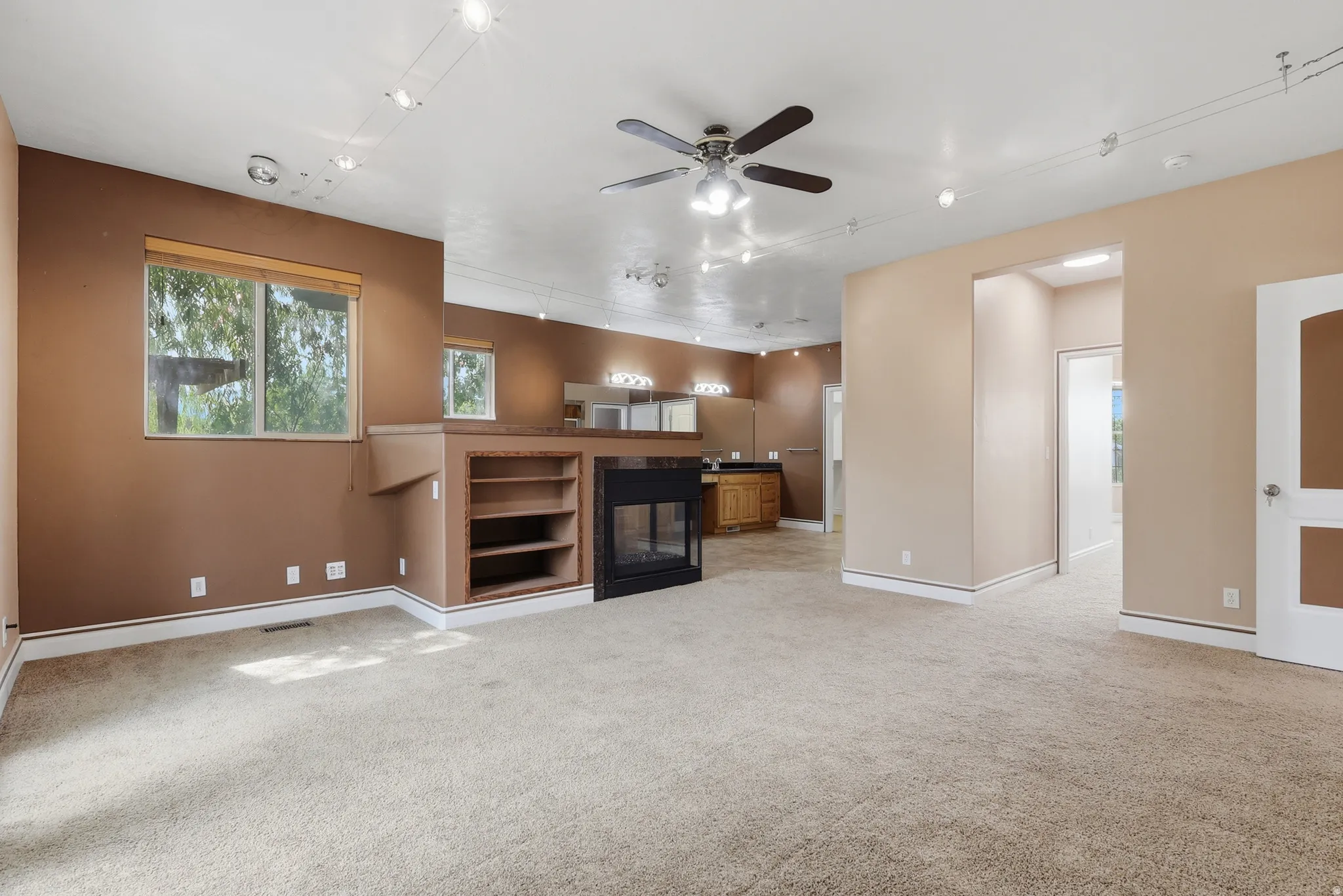 Carpeted interior space featuring track lighting, a ceiling fan, and built-in shelving
