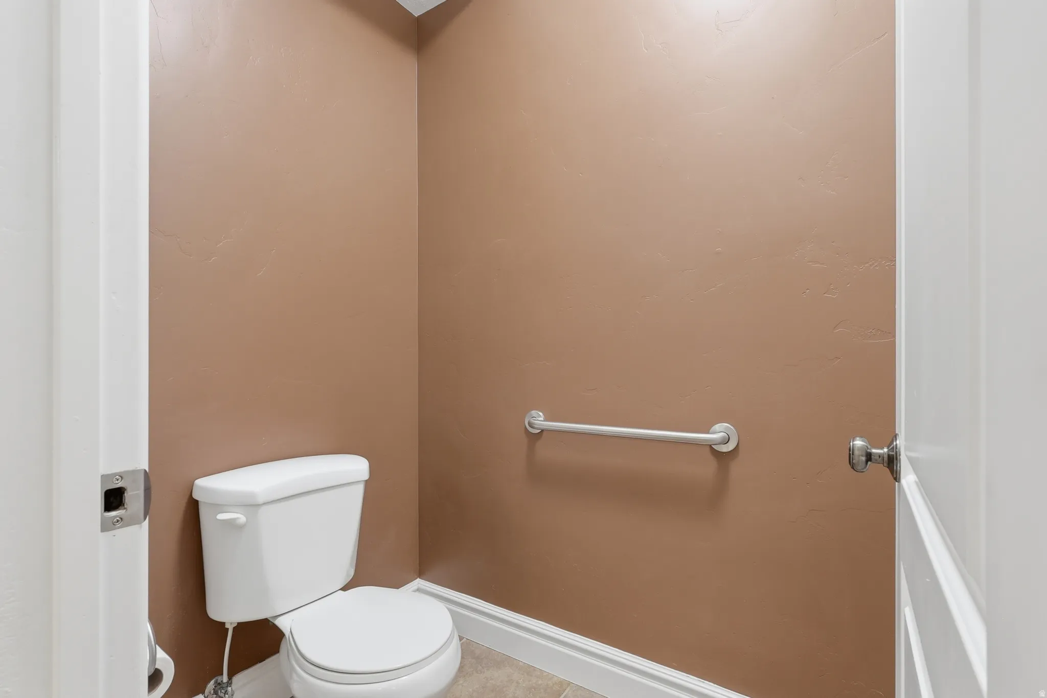 Compact water closet featuring a white toilet, neutral wall color, and a chrome grab bar
