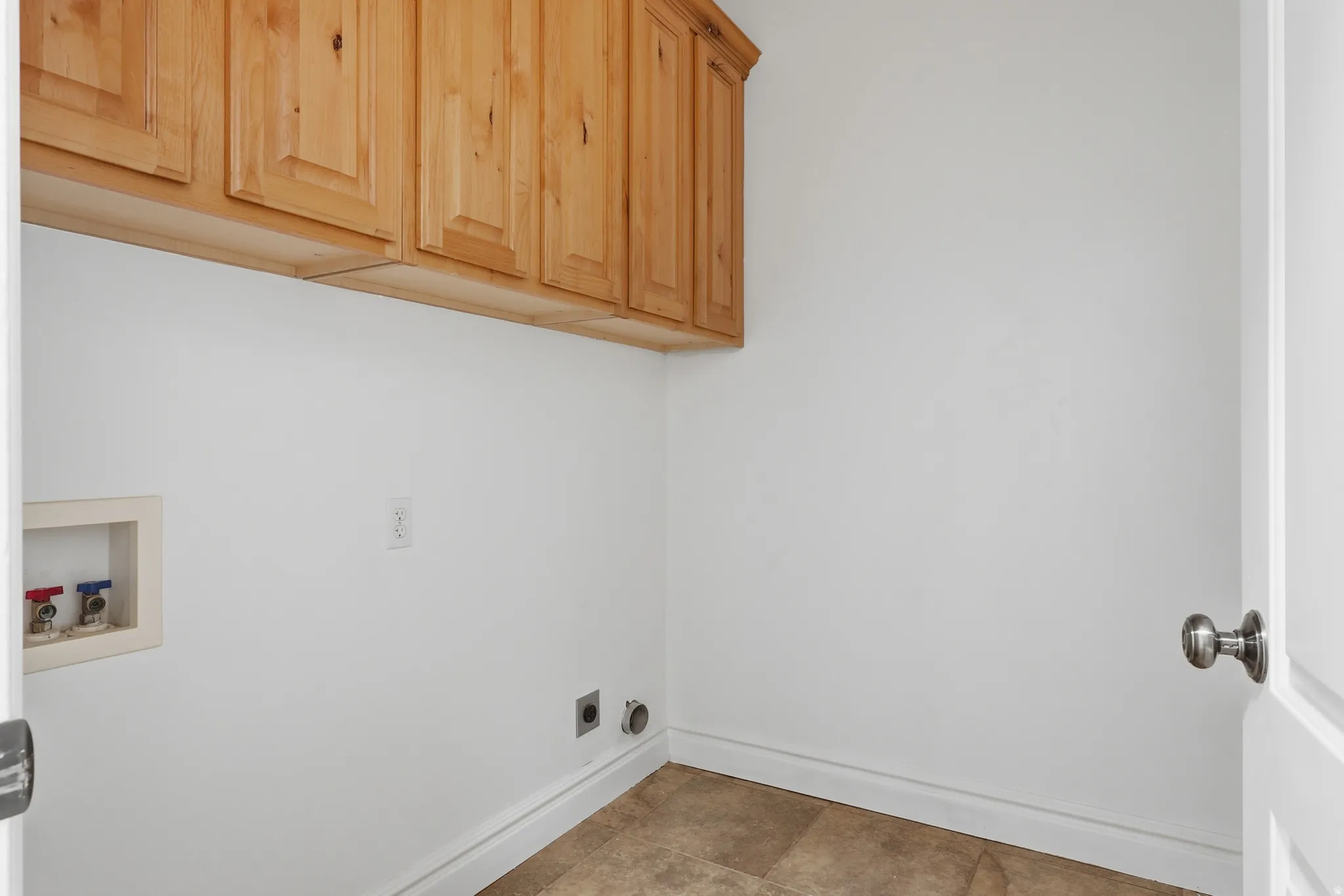 Laundry area featuring light wood cabinetry, white walls, and neutral tile flooring