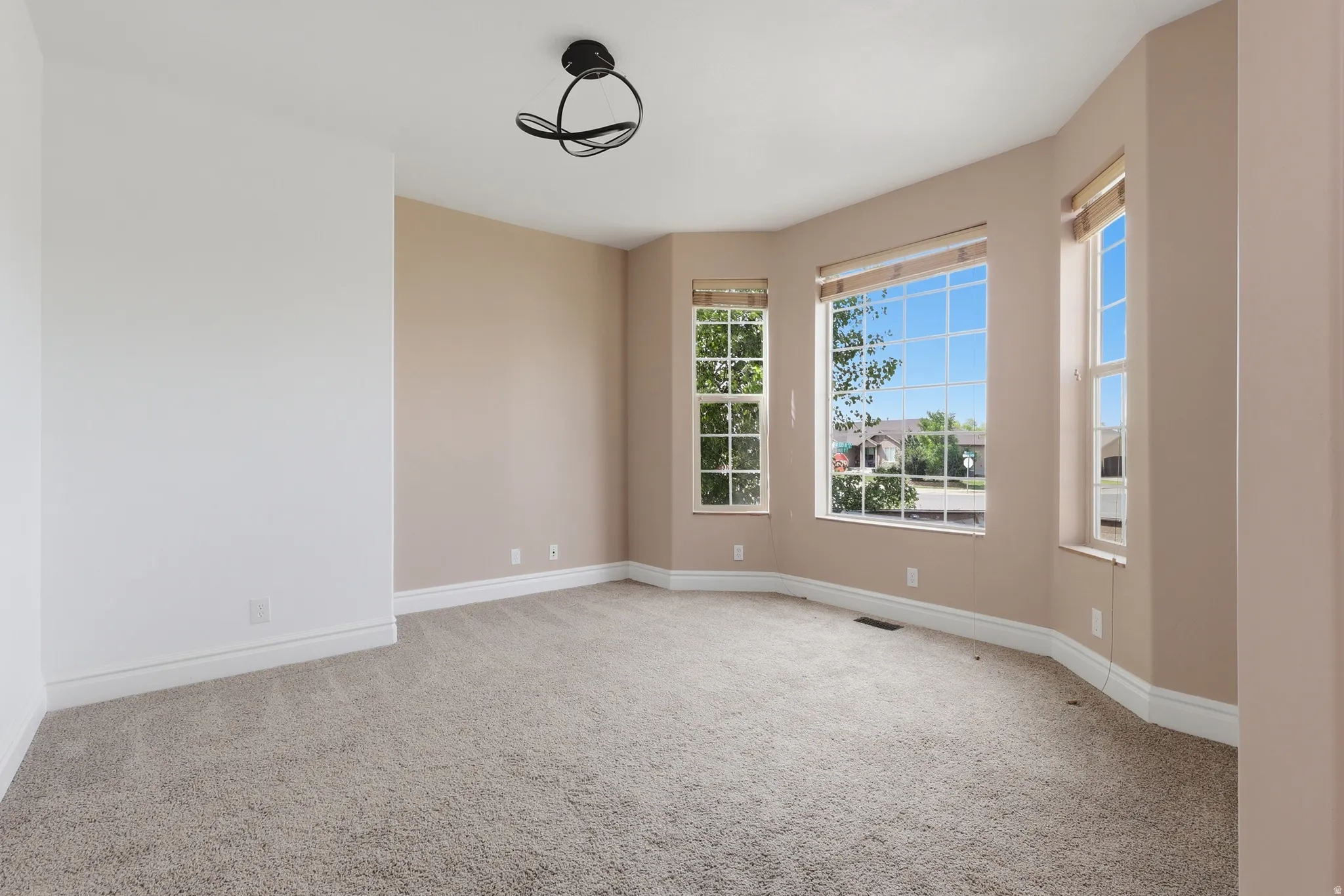 Bay window with multiple glass panes, light beige wall paint, neutral carpet flooring, white baseboards, and a contemporary ceiling light fixture