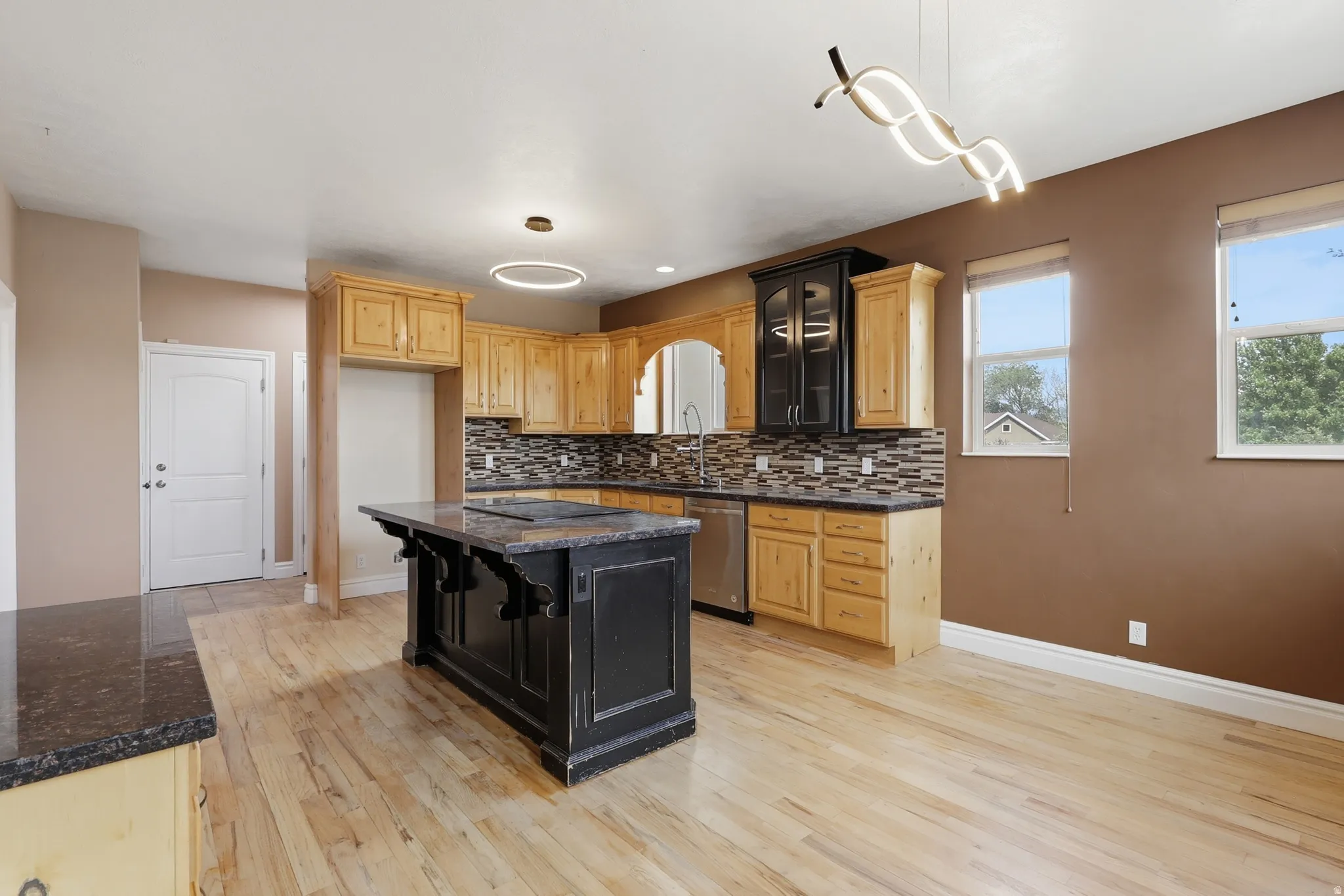 Spacious kitchen featuring light wood cabinetry, granite countertops, a decorative tile backsplash, stainless steel appliances, and a central island with a contrasting dark finish
