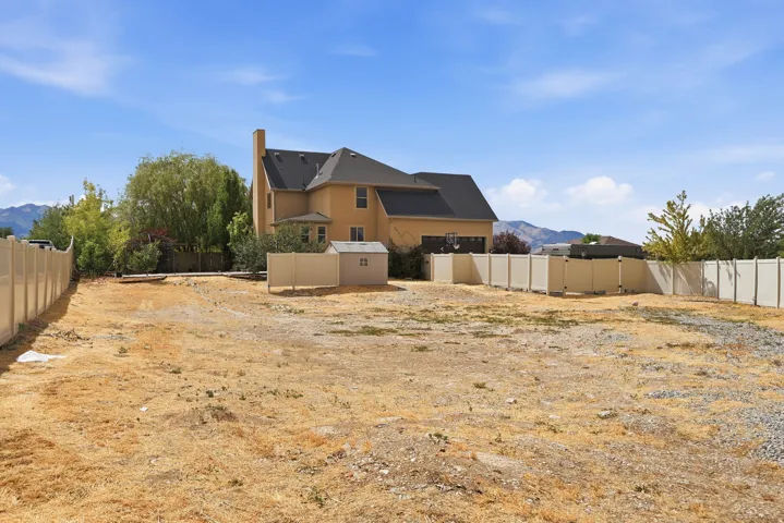 Expansive lot featuring a tan vinyl perimeter fence, a detached shed, mountain scenery, and a two-story residence in the background