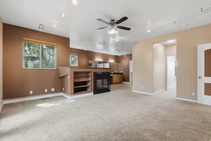 Carpeted interior space featuring track lighting, a ceiling fan, and built-in shelving