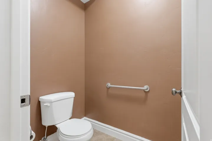Compact water closet featuring a white toilet, neutral wall color, and a chrome grab bar