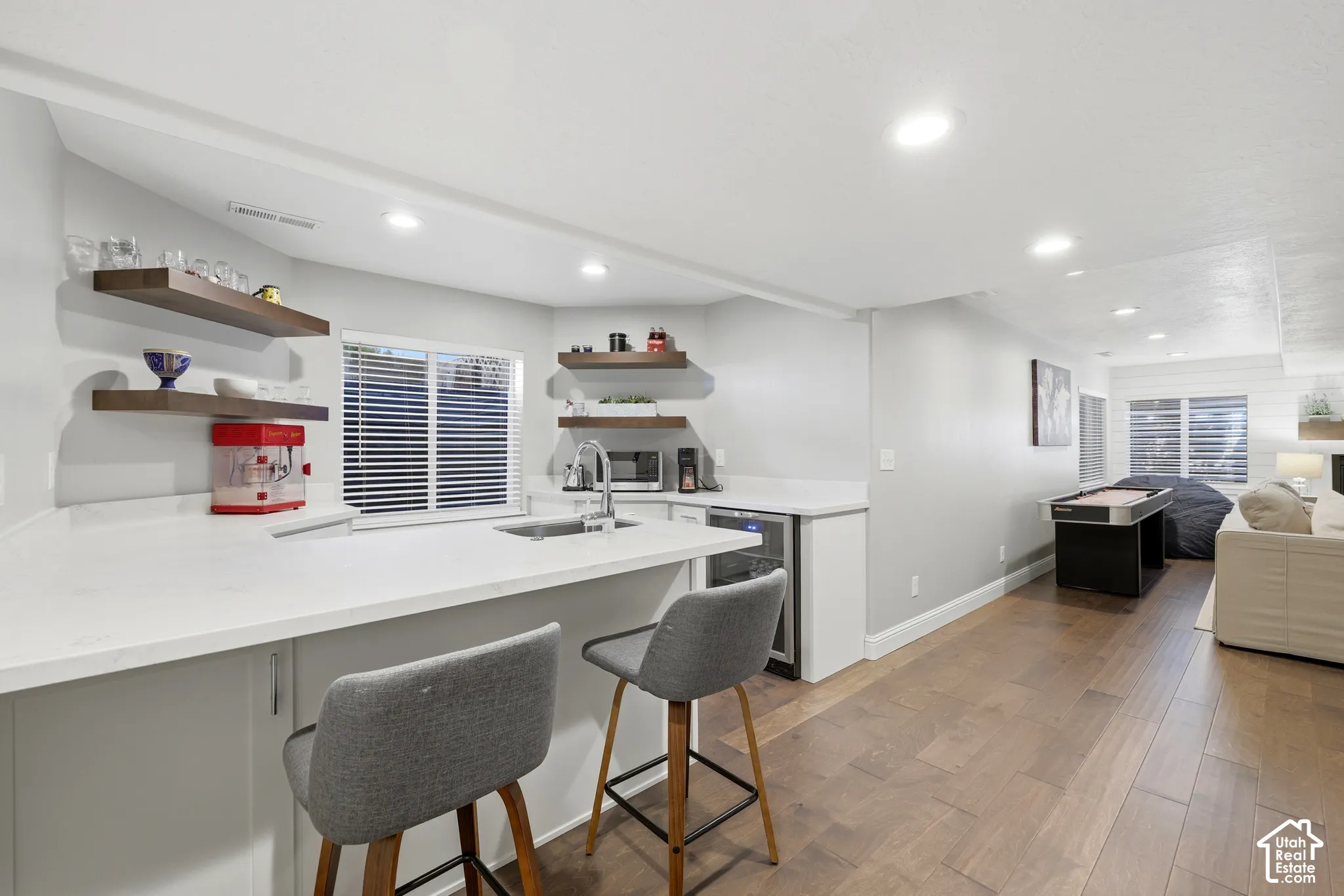 Kitchenette featuring white cabinetry, light-toned countertops, a stainless steel sink with a gooseneck faucet, and a beverage cooler