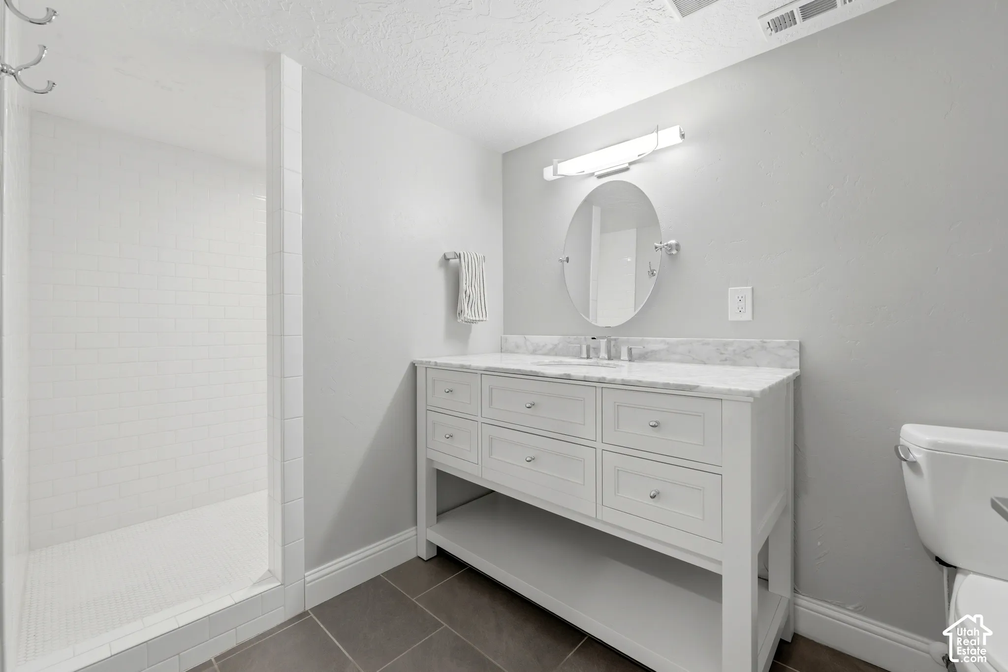 Bathroom featuring a white vanity with a stone countertop, an oval mirror, and a walk-in shower with white subway tile