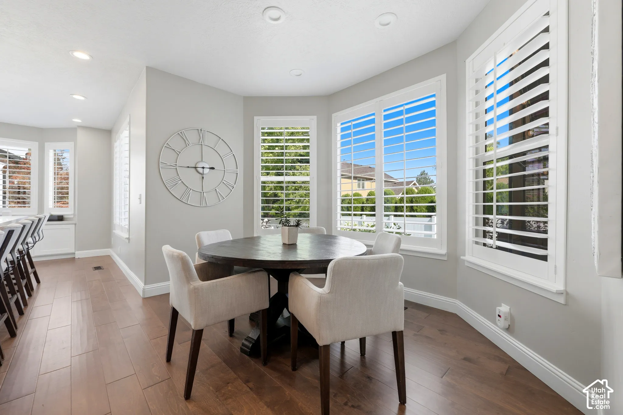 Bay window dining area featuring multiple windows with white plantation shutters, recessed lighting, wood-finish flooring, and light gray wall paint