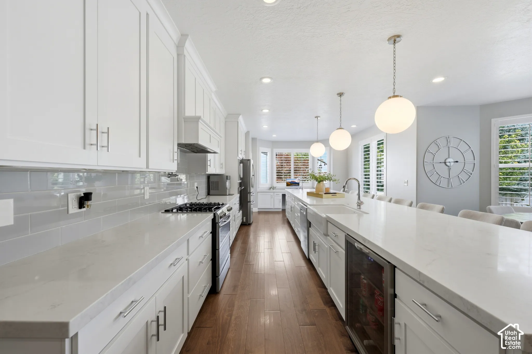 Spacious kitchen featuring white cabinetry, light countertops, wood-finish flooring, a built-in range, and a large island with pendant lighting and an integrated beverage cooler