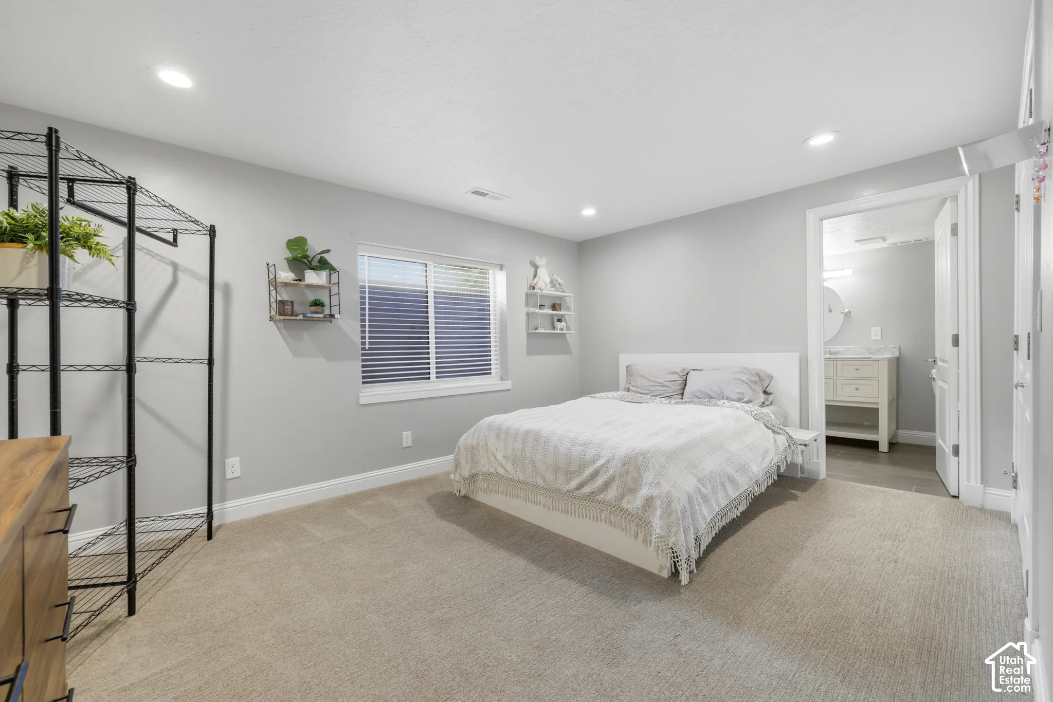 Carpeted room featuring a window with blinds, recessed lighting, and a doorway opening to a bathroom with a vanity