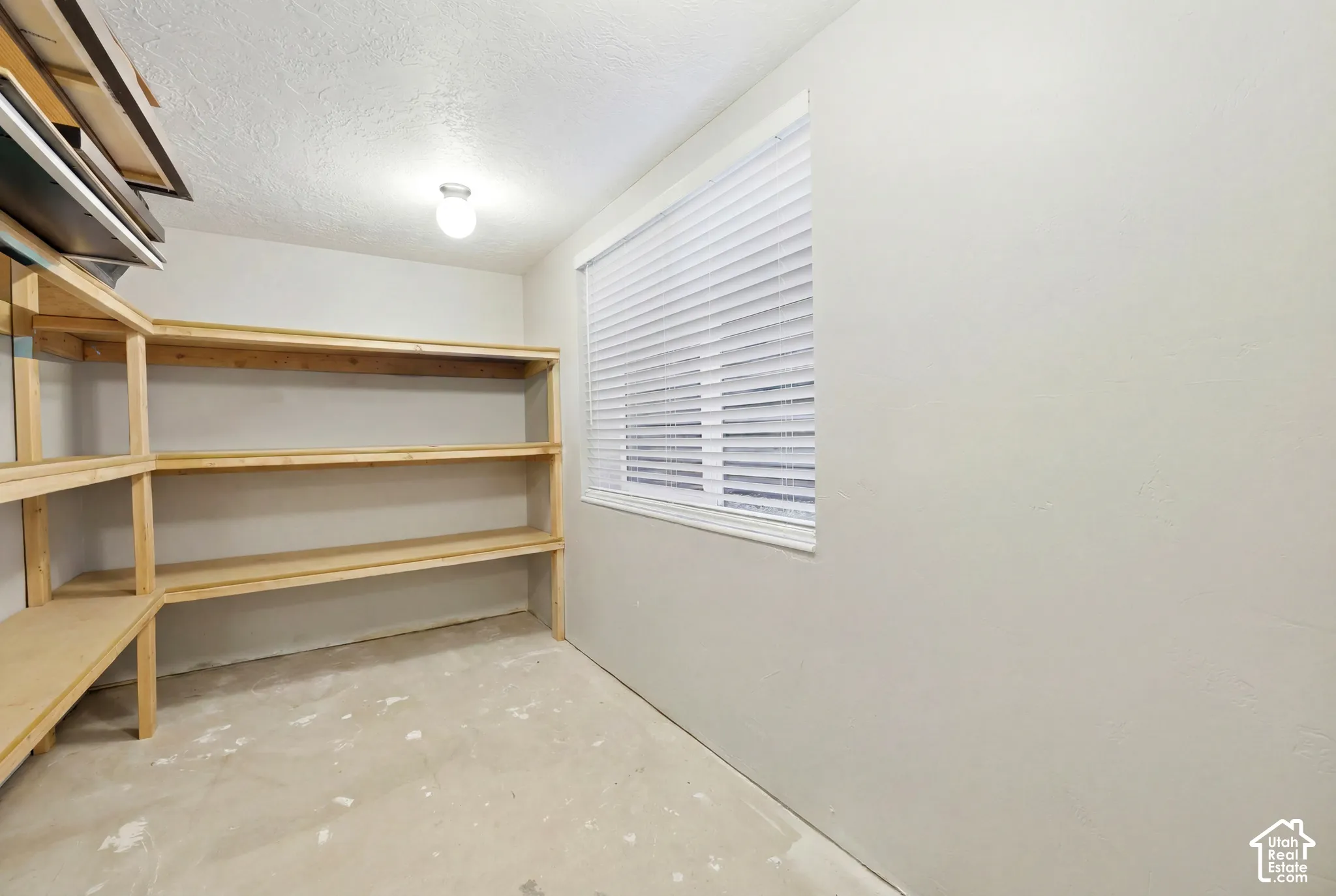 Dedicated storage room featuring extensive built-in wooden shelving, a window with horizontal blinds, and a neutral wall finish