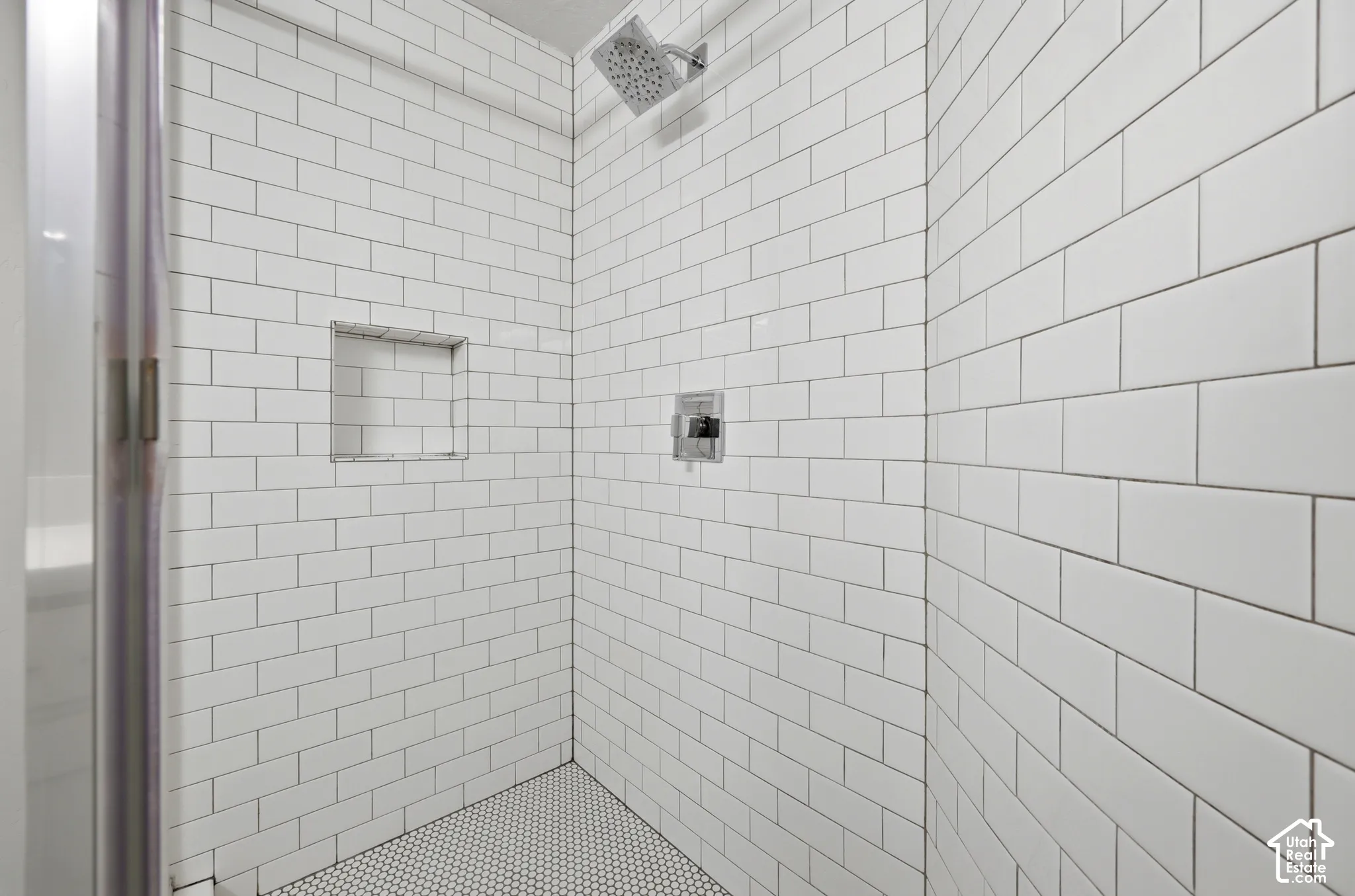 Shower enclosure featuring white subway tile walls, a built-in shower niche, and a contrasting penny tile shower floor