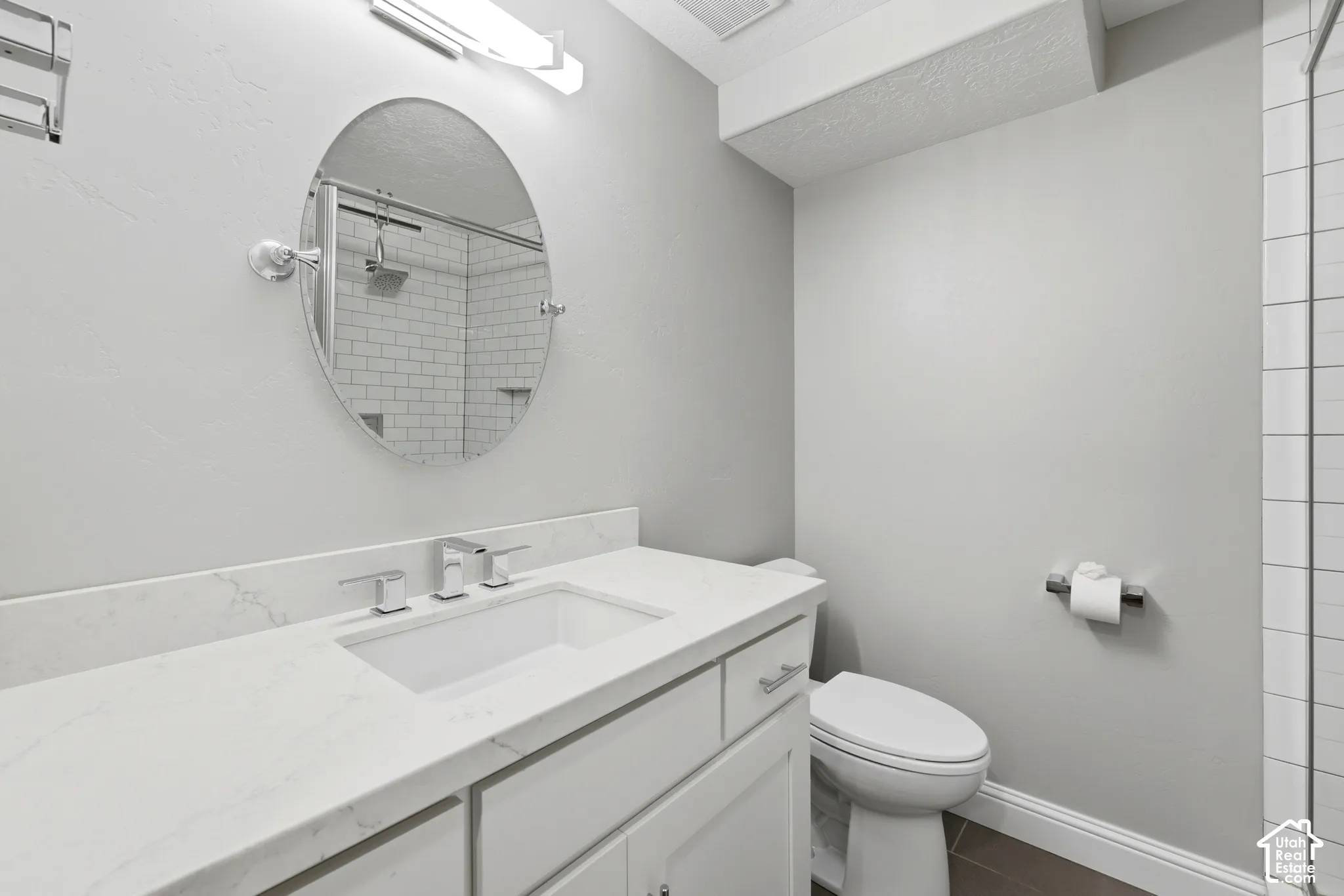 Bathroom featuring a white vanity with an undermount sink and polished chrome faucet, an oval mirror, and subway tile shower surround