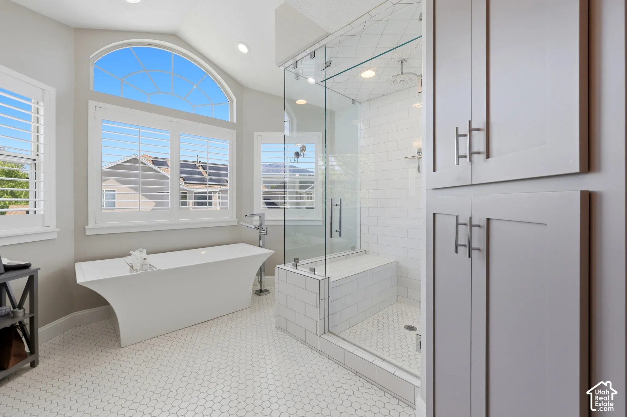 Modern bathroom featuring a freestanding tub, glass-enclosed shower with subway tile, honeycomb tile flooring, and integrated built-in cabinetry