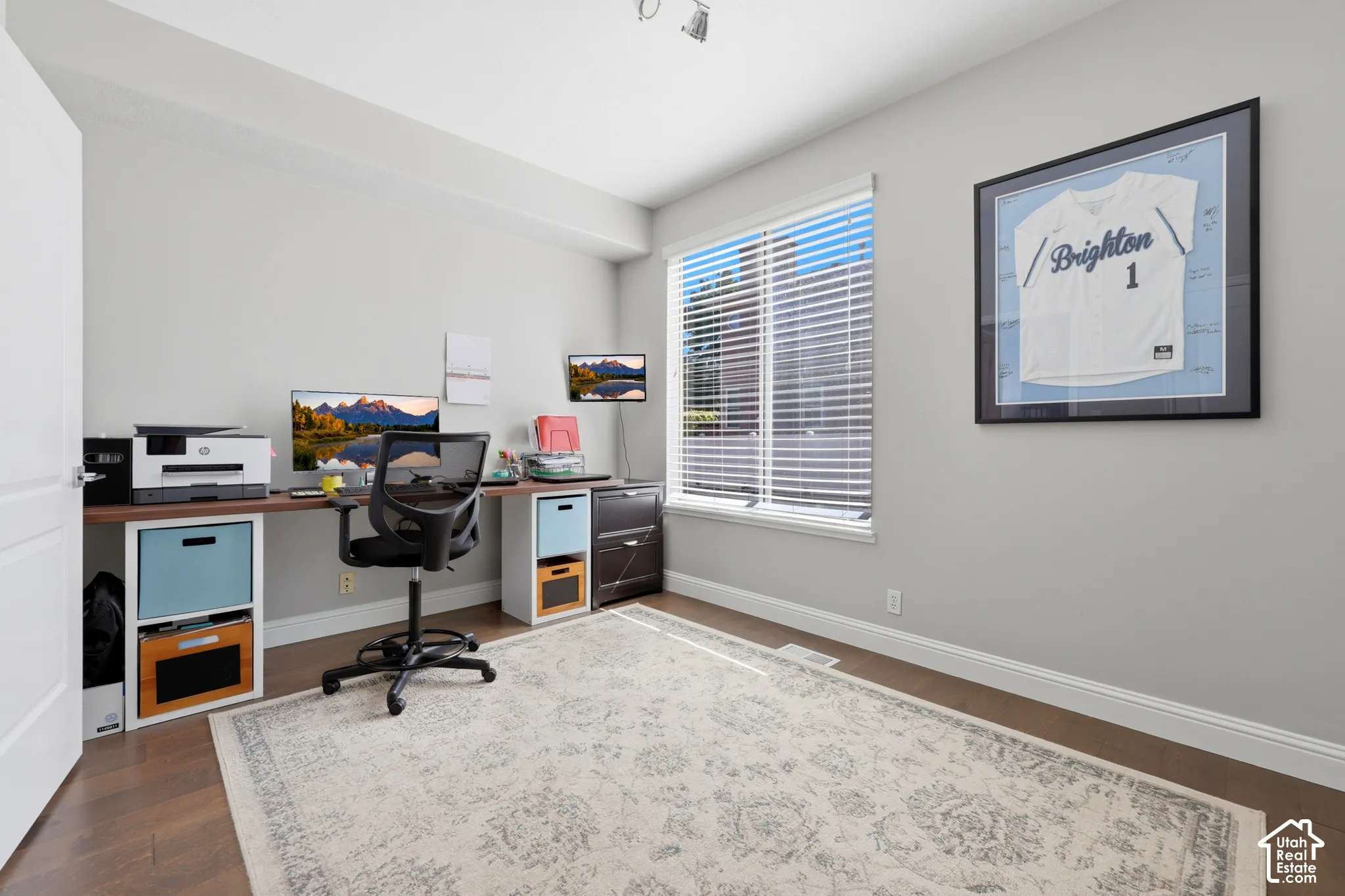 Bright room with light gray walls, wood-finish flooring, and a single window with horizontal blinds
