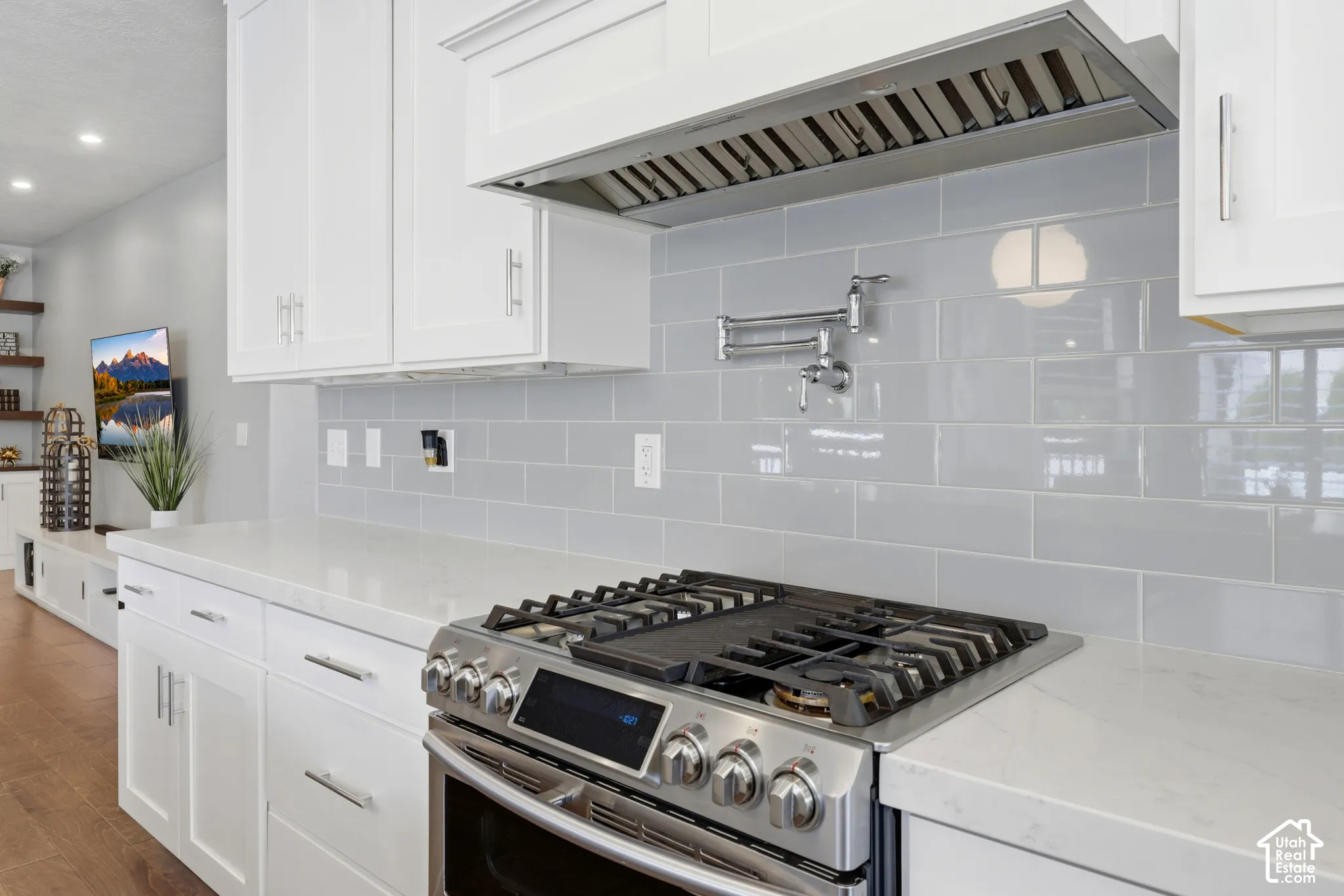 Modern kitchen featuring white shaker cabinetry, light-toned countertops, and a stainless steel gas range with a coordinating range hood