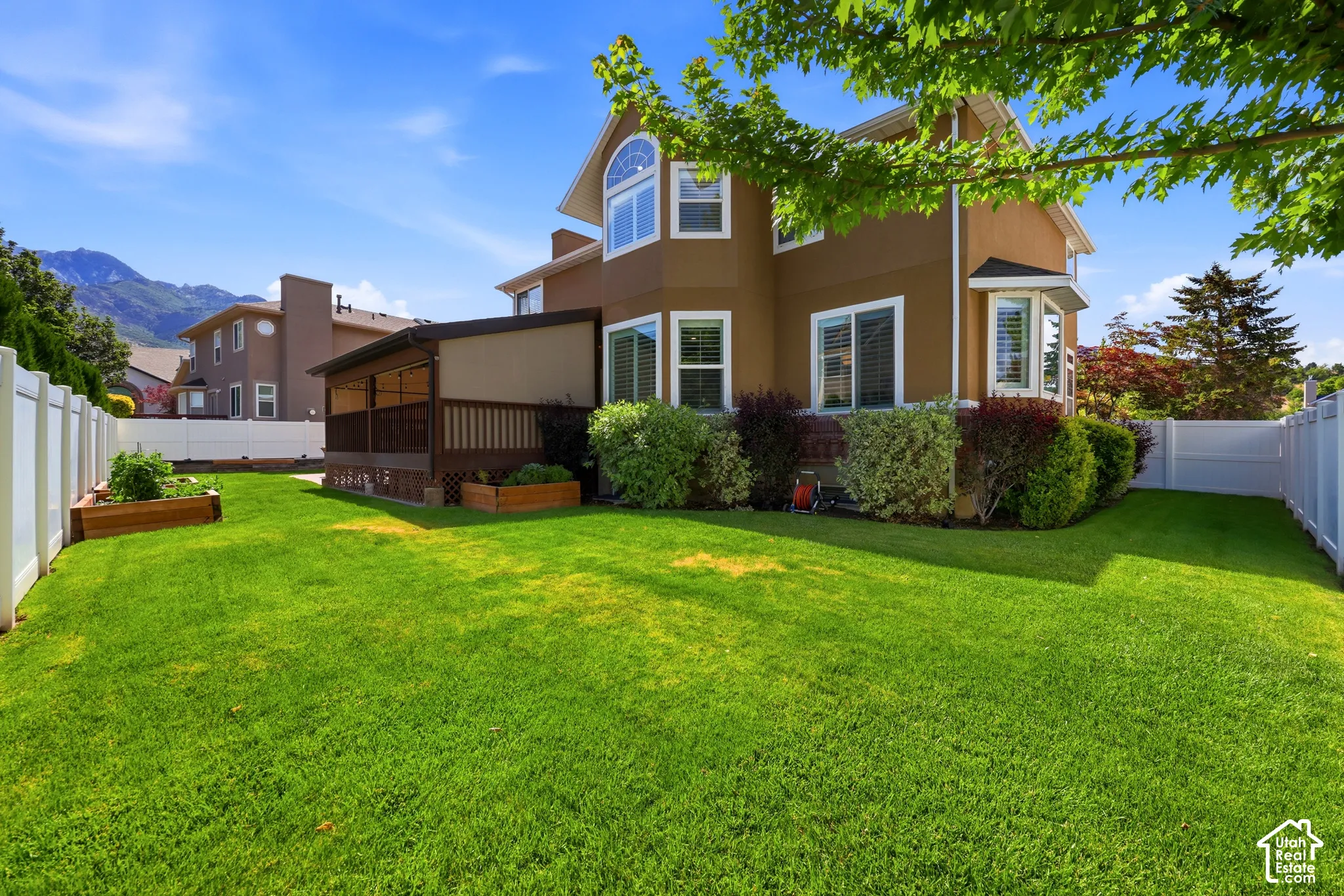 Expansive fenced backyard featuring a covered deck, raised garden beds, and mature landscaping