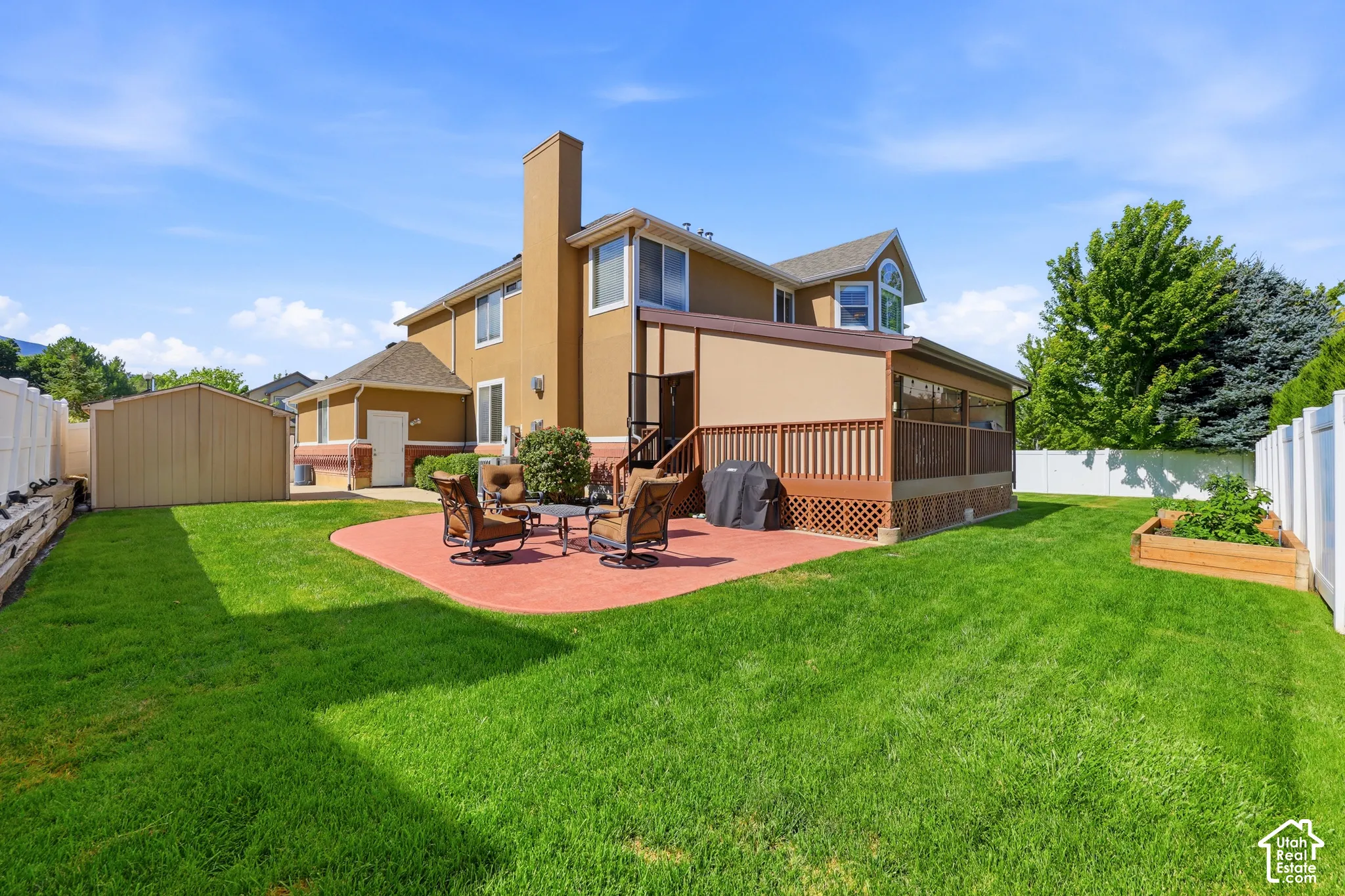 Expansive backyard featuring a red paver patio, a raised wood deck with privacy screen, and a storage shed