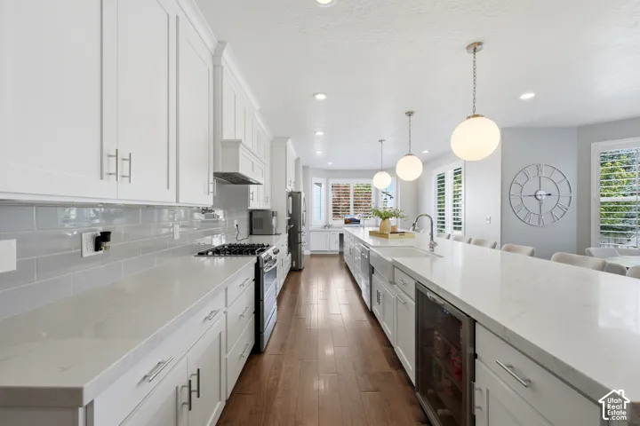 Spacious kitchen featuring white cabinetry, light countertops, wood-finish flooring, a built-in range, and a large island with pendant lighting and an integrated beverage cooler