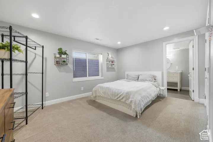 Carpeted room featuring a window with blinds, recessed lighting, and a doorway opening to a bathroom with a vanity