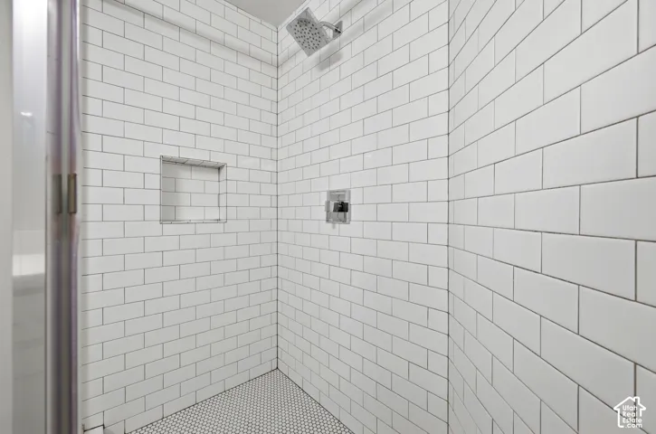 Shower enclosure featuring white subway tile walls, a built-in shower niche, and a contrasting penny tile shower floor