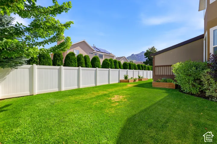 Expansive backyard featuring a manicured lawn, white privacy fencing, and mature perimeter shrubs
