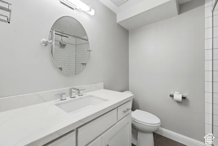Bathroom featuring a white vanity with an undermount sink and polished chrome faucet, an oval mirror, and subway tile shower surround