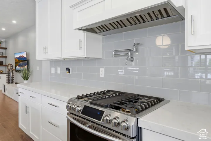 Modern kitchen featuring white shaker cabinetry, light-toned countertops, and a stainless steel gas range with a coordinating range hood
