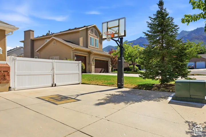 Concrete driveway with a movable basketball hoop, white privacy gate, and a mature evergreen tree