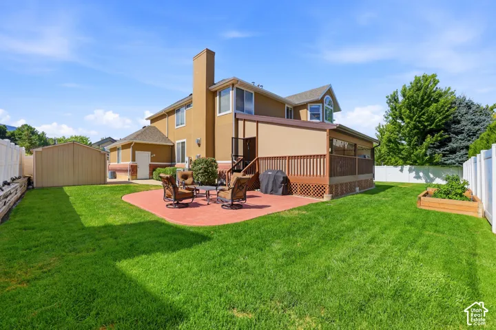Expansive backyard featuring a red paver patio, a raised wood deck with privacy screen, and a storage shed