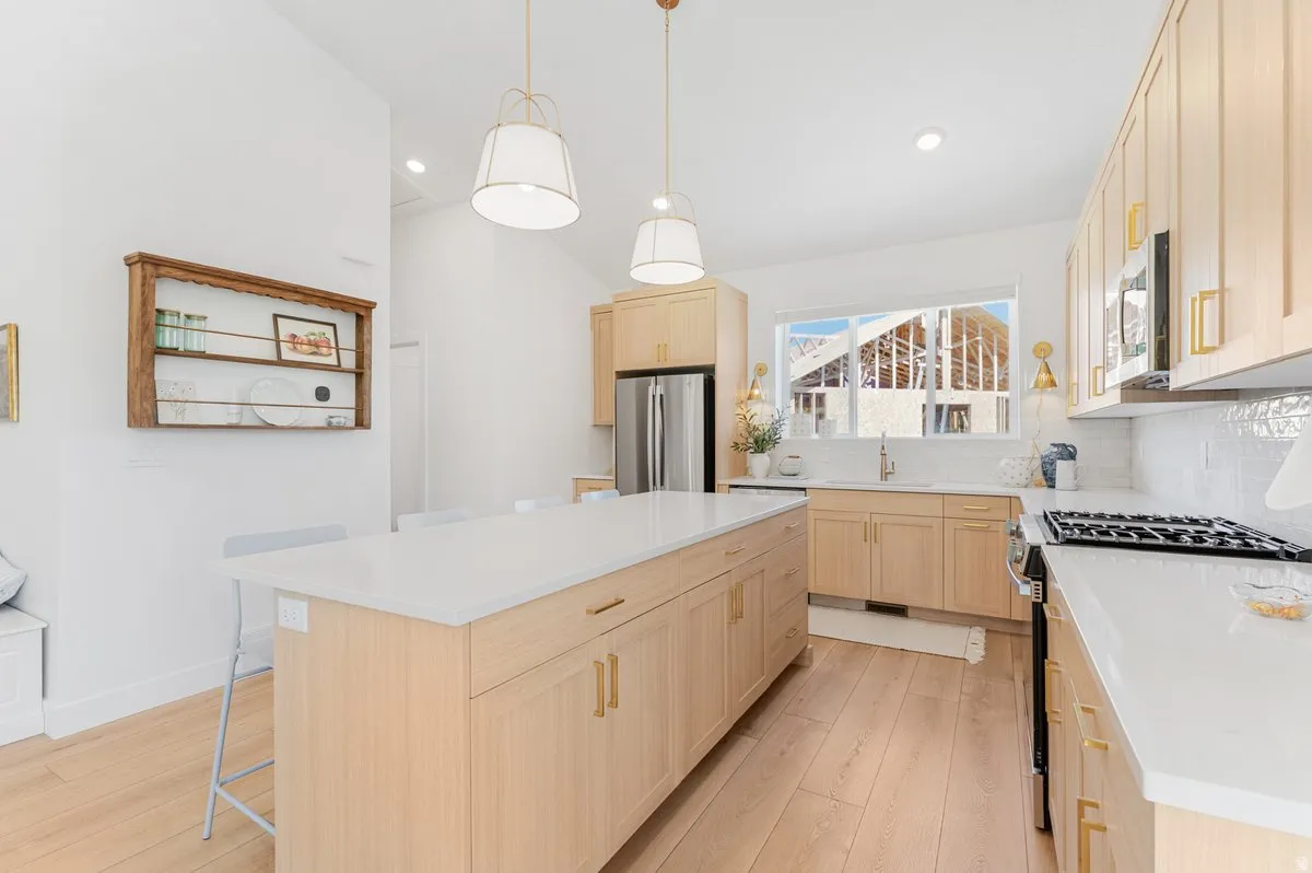 Bright kitchen featuring a large central island with seating, light wood-finish cabinetry, stainless steel appliances, white countertops, and wood-finish flooring