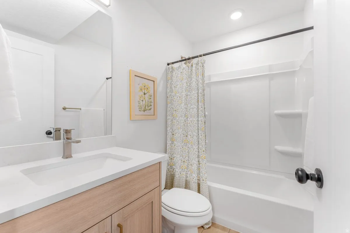 Bathroom featuring a light wood-finish vanity with a white countertop and undermount sink, a chrome faucet, a rectangular mirror, and a white tub/shower combination with an integrated shelving unit
