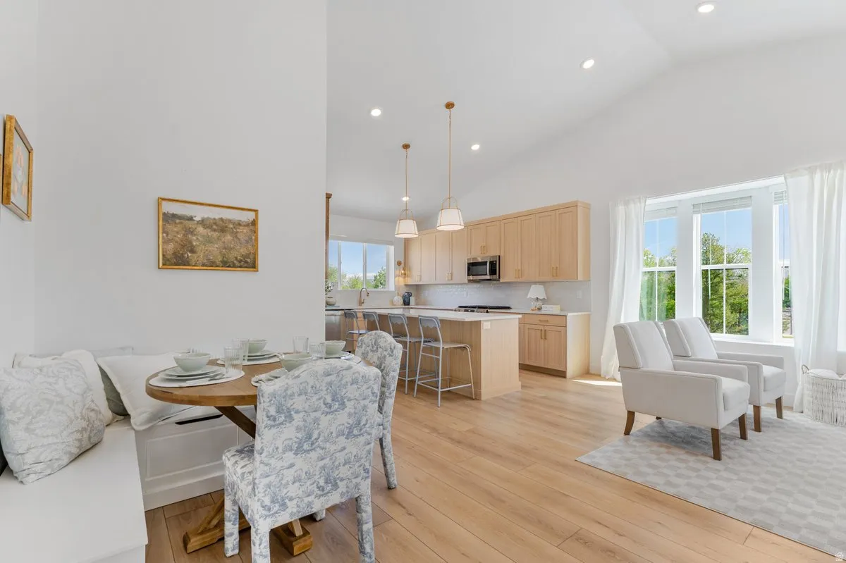Vaulted ceiling in an open-concept living area featuring light wood-finish flooring, a kitchen with light wood cabinetry, a central island with bar seating, and a dining nook with built-in bench seating