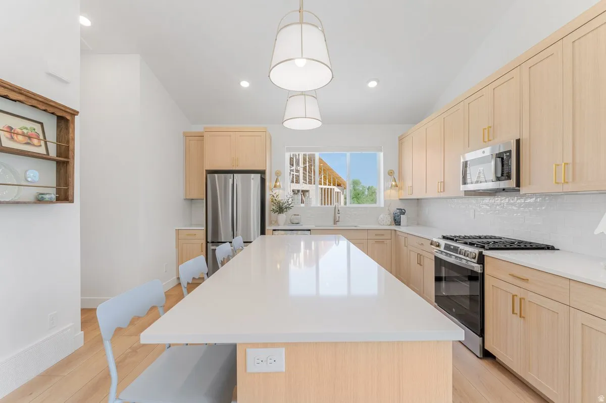 Kitchen featuring a large central island, light wood-finish cabinetry, a stainless steel gas range, a stainless steel microwave, and white subway tile backsplash