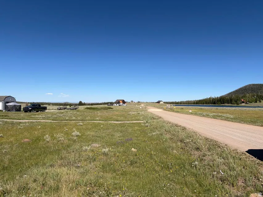 Expansive open land featuring a gravel road, distant lake, and surrounding evergreen-covered hills