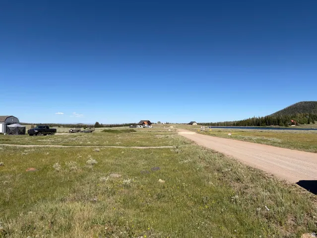 Expansive open land featuring a gravel road, distant lake, and surrounding evergreen-covered hills