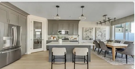 Open-concept kitchen and dining area featuring light wood-finish flooring, gray shaker cabinetry, and a central island with a light-colored countertop. PICTURE IS OF A SIMILAR HOME