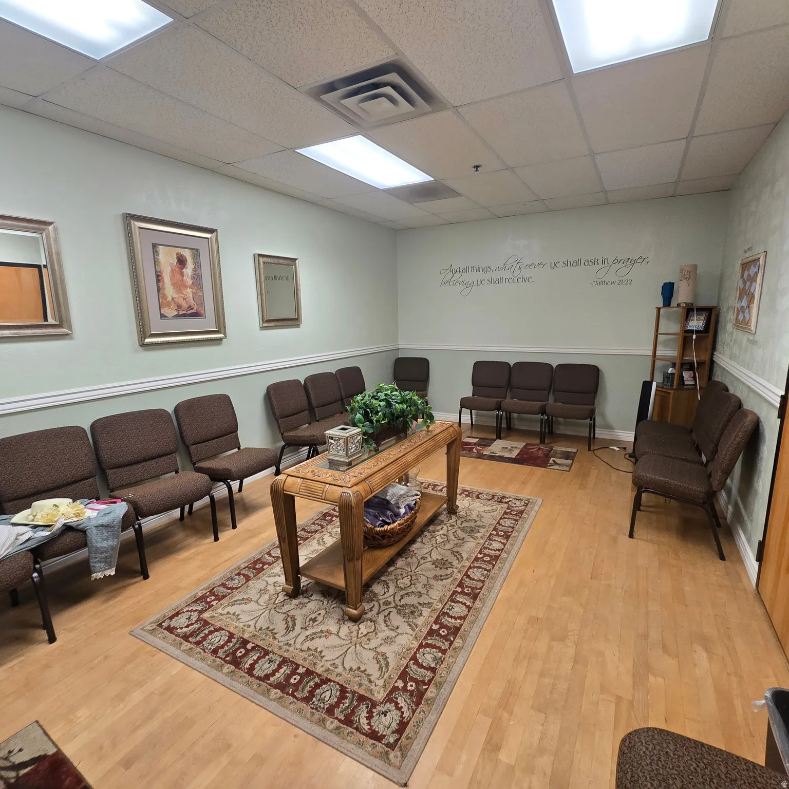 Spacious waiting area featuring light wood-finish flooring, a drop ceiling with recessed lighting, and pale green walls with white chair rail molding