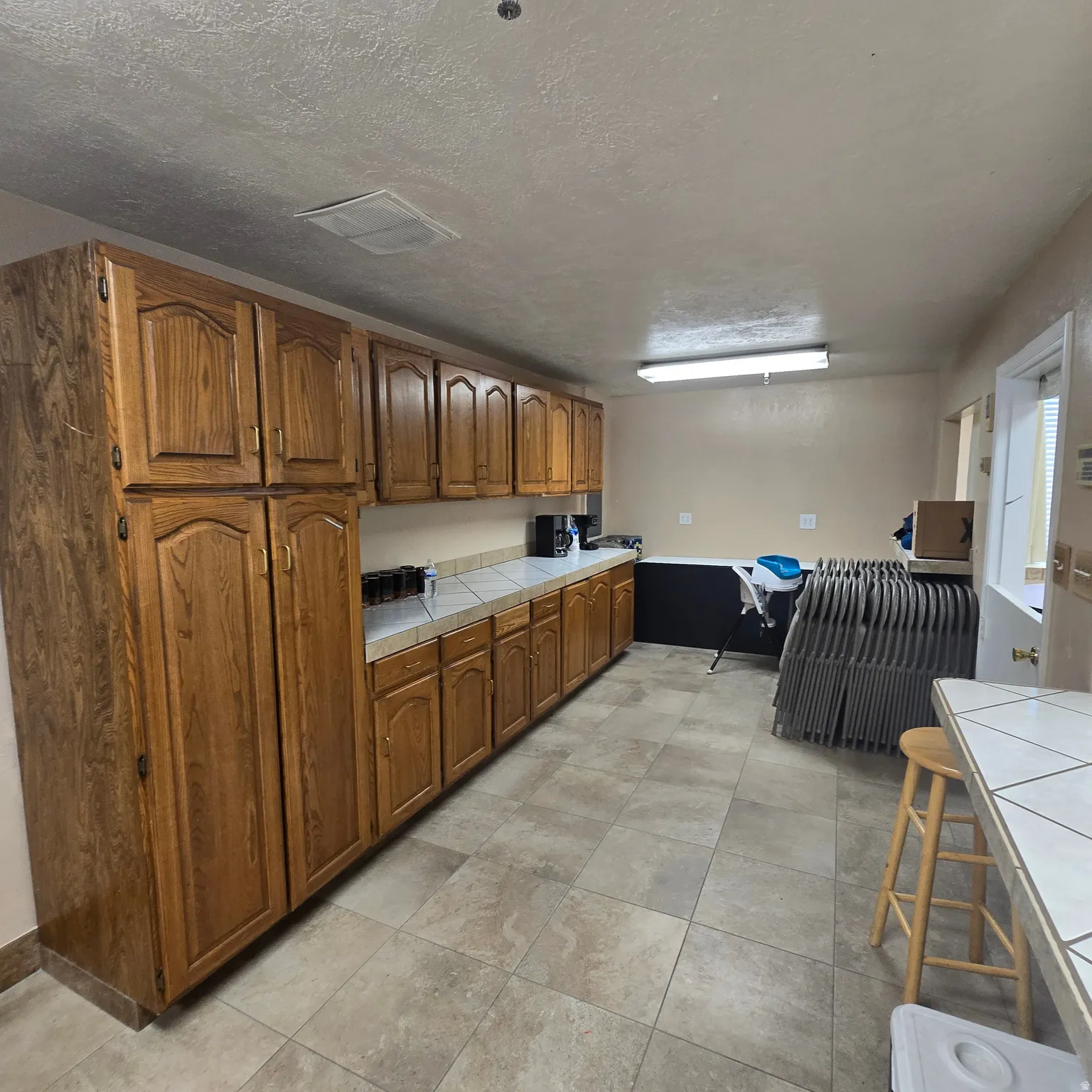 Kitchen prep area featuring extensive wood cabinetry, tile countertops, and neutral-toned floor tile